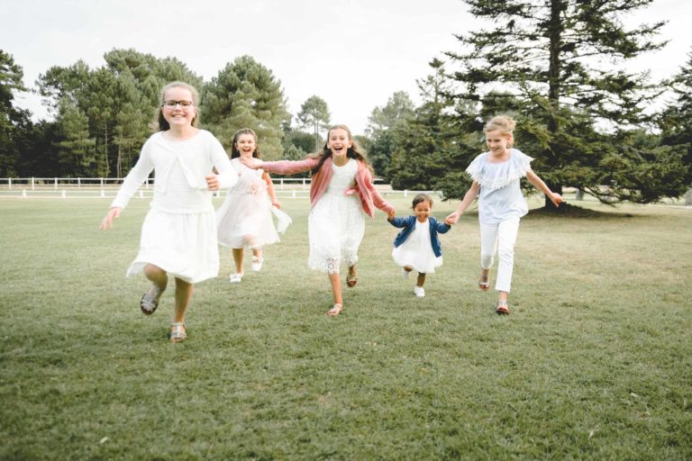 Cinq enfants courent vers la caméra en souriant et en riant. Vêtus de tenues d'été aux couleurs claires, ils incarnent la simplicité de l'enfance alors qu'ils jouent sur un terrain gazonné entouré d'arbres. Le ciel est clair, laissant présager d'une journée ensoleillée. L'image capture un moment joyeux et ludique marqué par une véritable générosité entre amis.