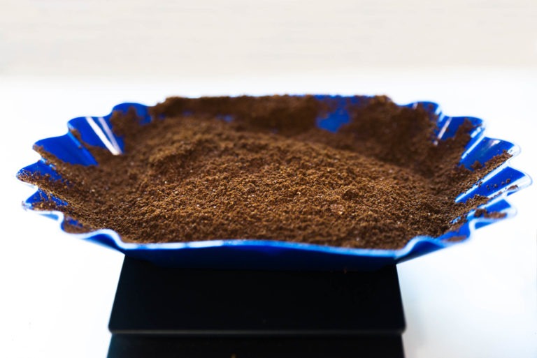 Gros plan sur du café moulu présenté dans un plat ondulé en céramique bleu cobalt. La texture fine et la riche couleur brune du café torréfacteur bio équitable de Café Michel sont mises en valeur. Le plat contraste avec le fond neutre et est placé sur une plateforme noire.