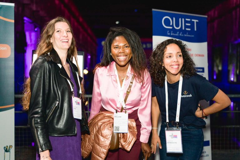 Trois femmes se tiennent debout, sourient et posent pour une photo lors de la French Tech Night 2024. Elles portent des cordons avec leur nom. La femme à droite porte une chemise bleu marine avec le texte « weecook » dessus. L'arrière-plan présente une bannière « QUIET » avec du texte supplémentaire. Le décor semble être en intérieur avec un éclairage coloré.